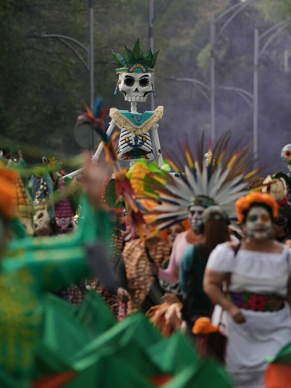 Cardboard skeletons dance, colorful floats roll: People in makeup and costumes celebrate Día de Muertos in Mexico City.